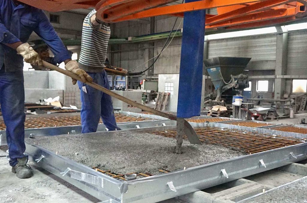Arbeiter gießen Beton in eine Form in einer Produktionshalle für Ingenieurbeton.