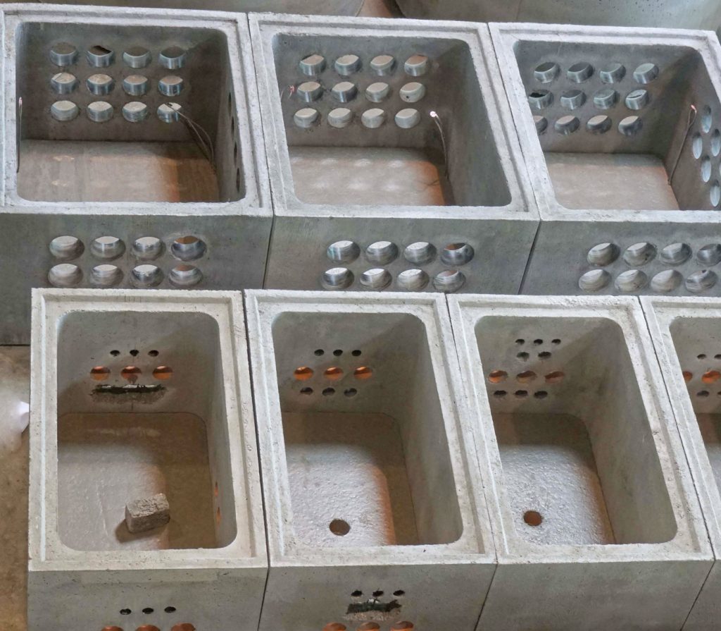 Reihe von grauen Betonblöcken mit gleichmäßig verteilten Löchern auf der Oberfläche.