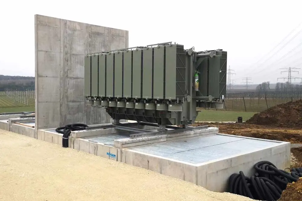 Transformatorstation auf einer Betonplatte mit einer grauen Wand im Hintergrund.