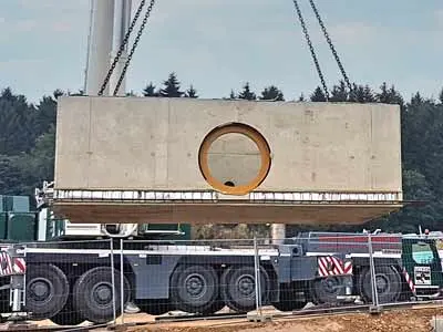 Eine große Betonplatte mit einer runden Öffnung wird von einem Kran angehoben.