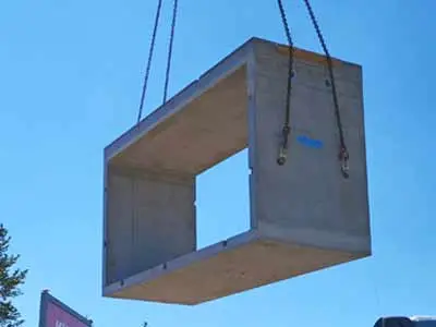 Ein Betonrahmen mit rechteckigem Durchlass wird von einem Kran in die Luft gehoben.