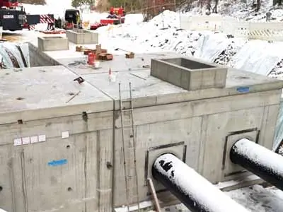 Betonwasserleitungsschacht mit zwei Rohren und einer Leiter auf der Oberfläche.