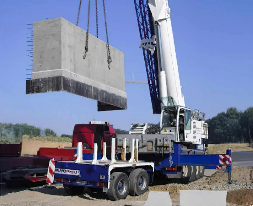 Ein Kran hebt einen großen Betonblock von einem Lkw auf einer Baustelle an.