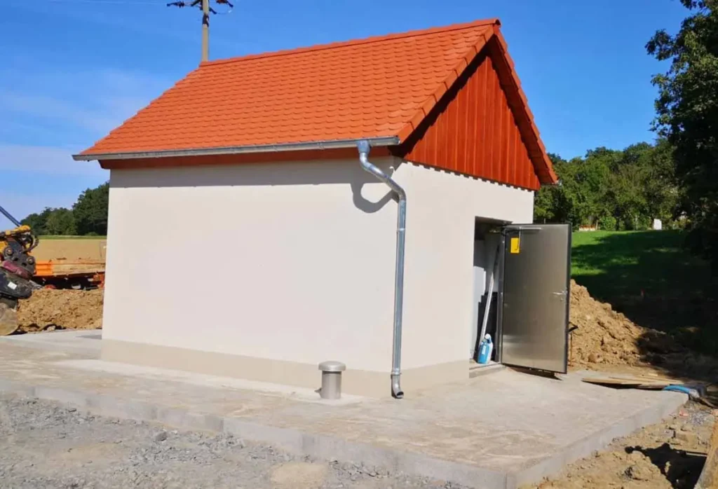 Ein Betriebsgebäude für Pumpwerke mit rotem Dach und grauer Fassade, ausgestattet mit einer Metalltür.