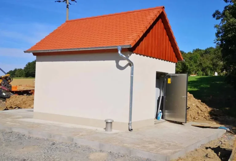 Ein Betriebsgebäude für Pumpwerke mit rotem Dach und grauer Fassade, ausgestattet mit einer Metalltür.