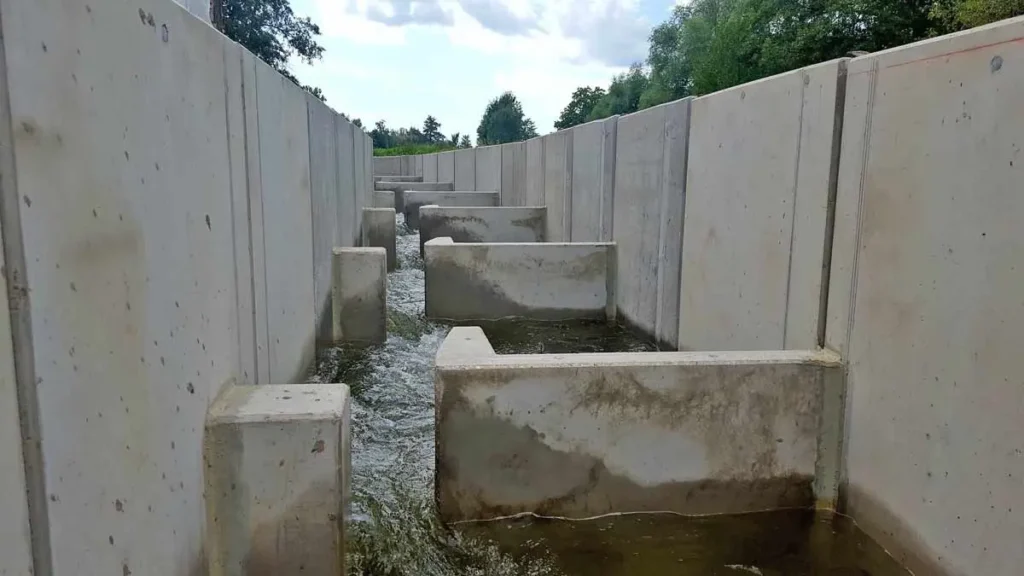 Betonfischtreppe mit Wasserlauf zwischen den Strukturen in einem geraden Kanal.
