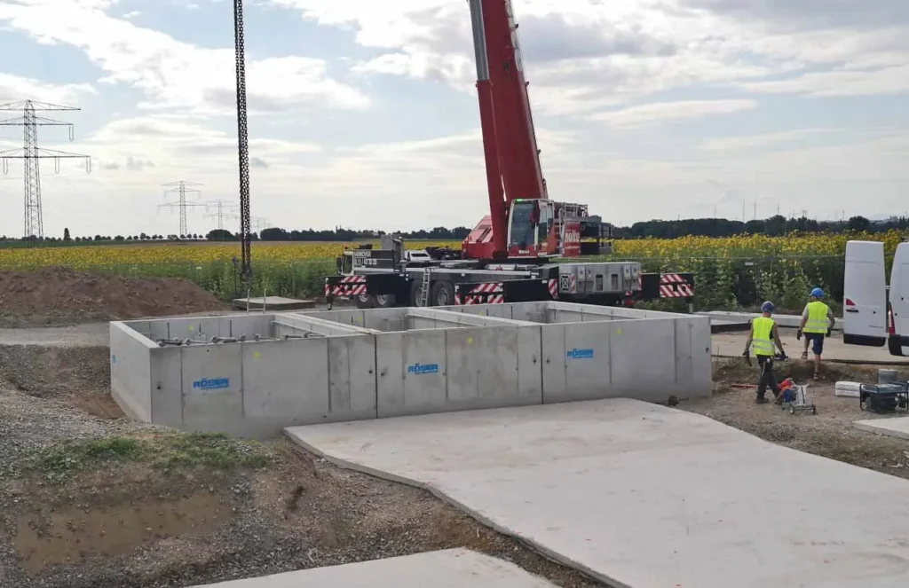 Betonfundamente auf einer Baustelle mit Bauarbeitern und einem Kran im Hintergrund.