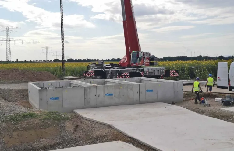 Betonfundamente auf einer Baustelle mit Bauarbeitern und einem Kran im Hintergrund.