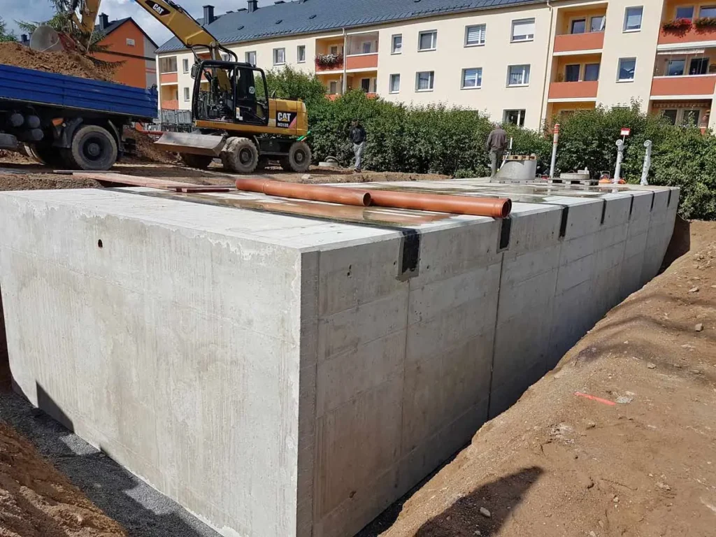 Betonlöschwasserbehälter auf einer Baustelle mit Baugeräten im Hintergrund.