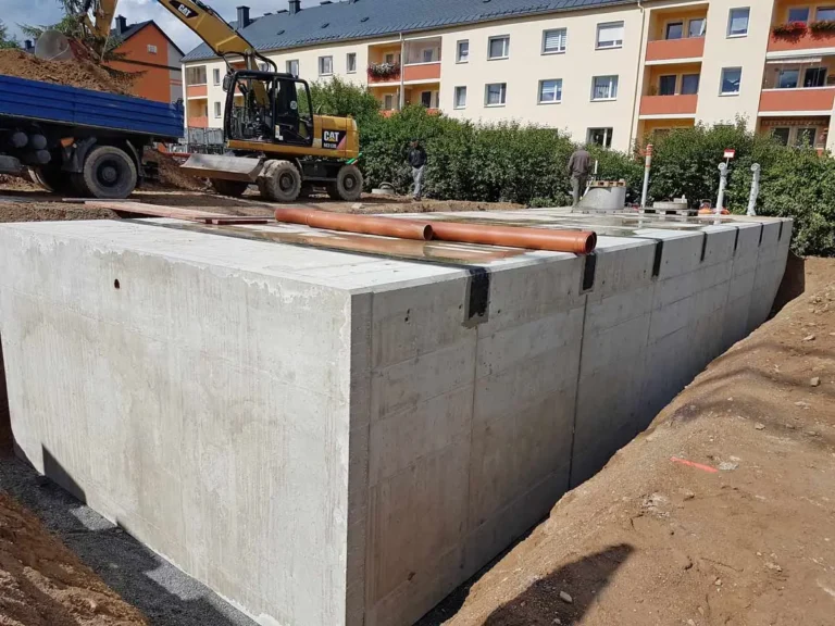 Betonlöschwasserbehälter auf einer Baustelle mit Baugeräten im Hintergrund.