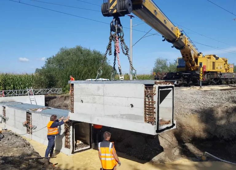Ein Kran hebt einen Betonrahmen an, während Arbeiter in Sicherheitswesten zuschauen.