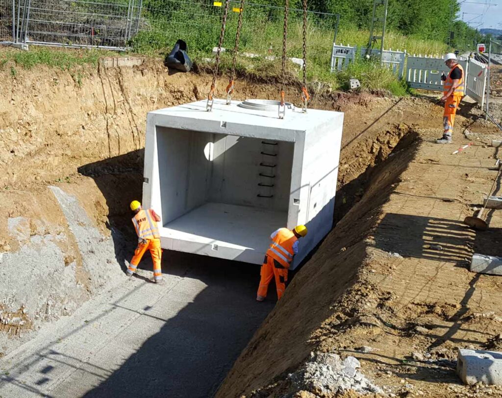 Zwei Bauarbeiter positionieren einen großen Betonbaukasten während der Installation eines Regenrückhaltebeckens.