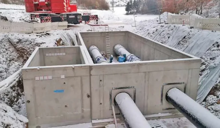 Betonbehälter mit zwei Trinkwasserleitungen, die in einem Schneegebiet installiert sind.