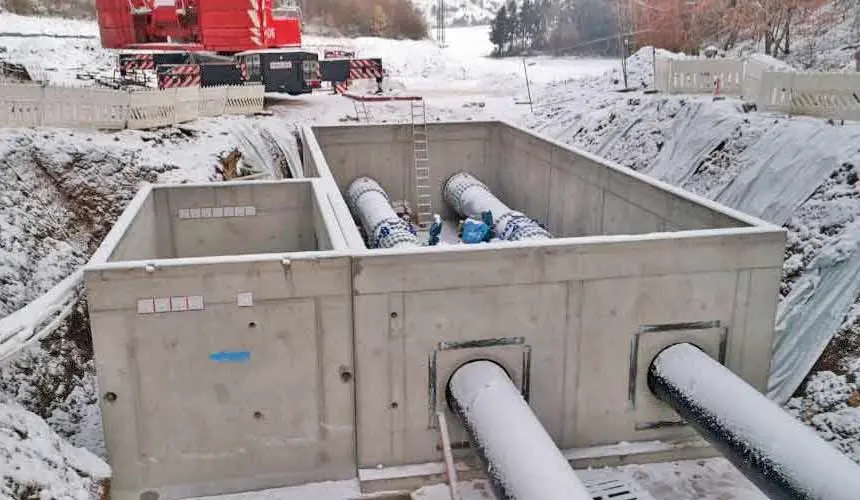 Betonbehälter mit zwei Trinkwasserleitungen, die in einem Schneegebiet installiert sind.