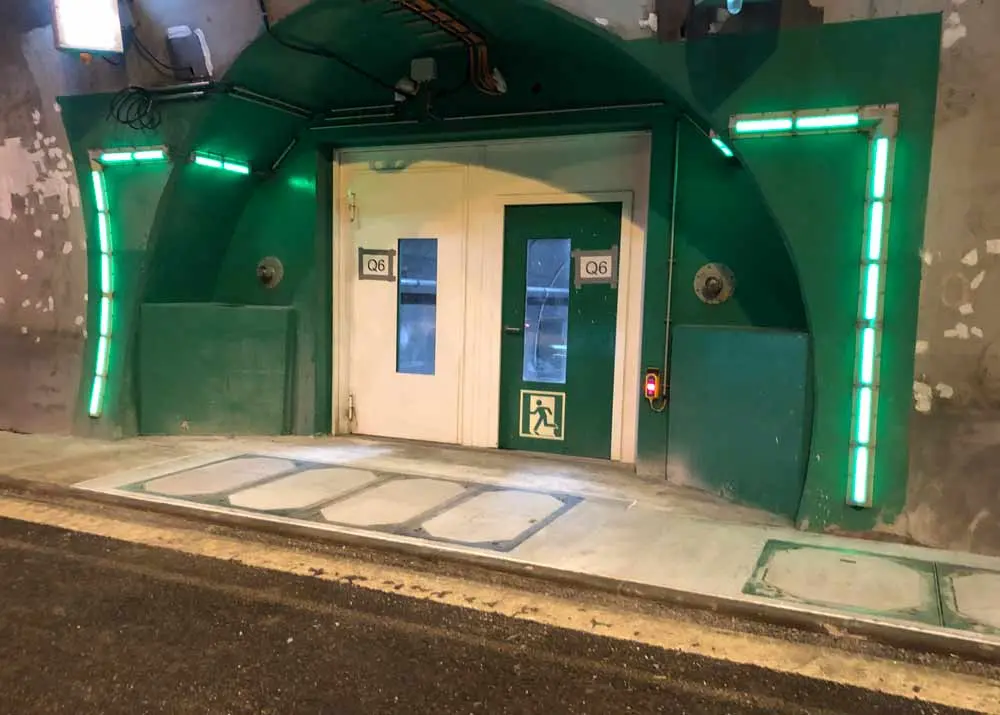 Grüner Tunnel mit einer Tür und Notausgangssymbol, beleuchtet von grünen Lichtern.